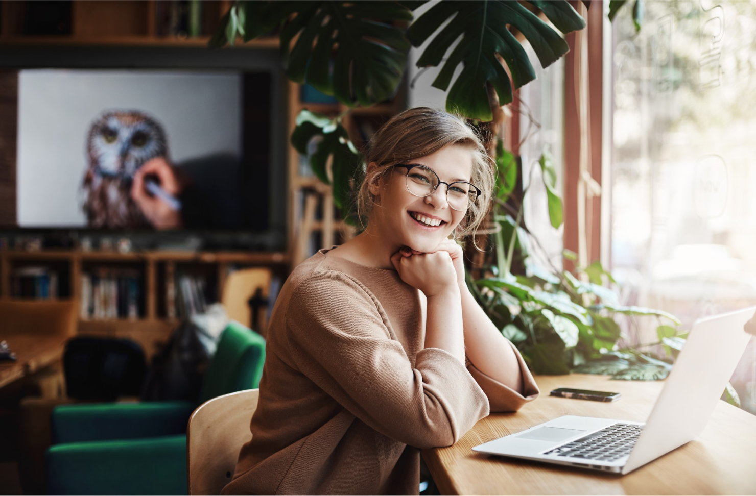Mujer con gafas y jersei beige sentada en un escritorio con un portátil gris, sonriendo en BarmetMedia.